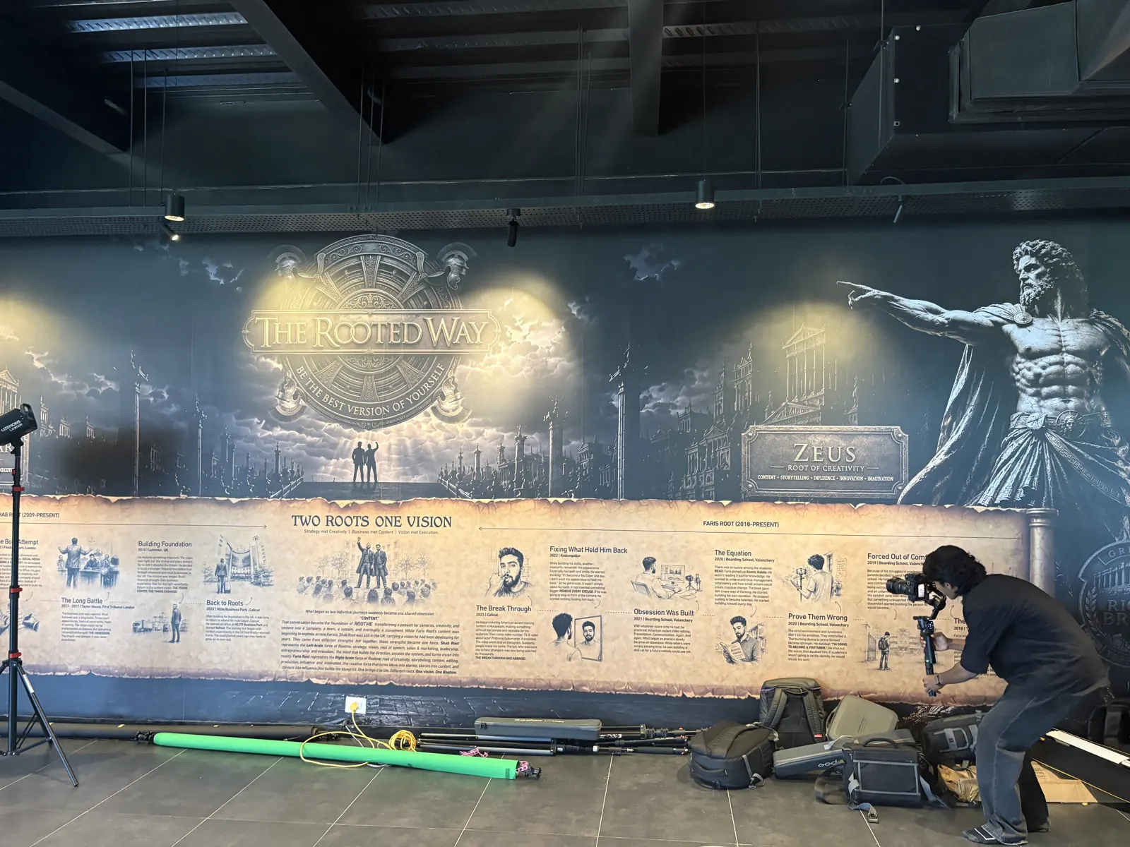 A student filming beside the Rootmedia mural — The Rooted Way, Two Roots One Vision